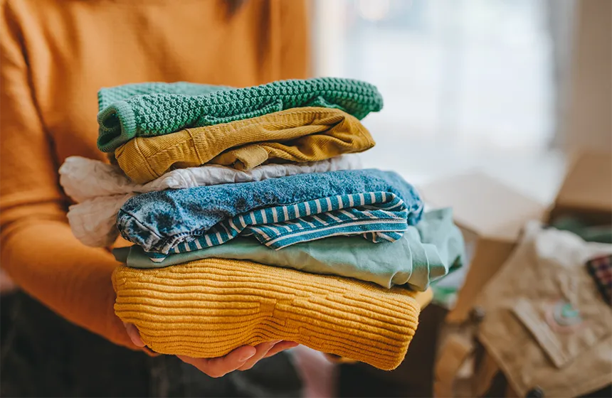 A person holding a pile of folded clothes ready to pack into a donation box